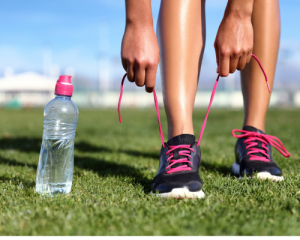 Person ties tennis shoes on grass with functional hydration bottled beverage