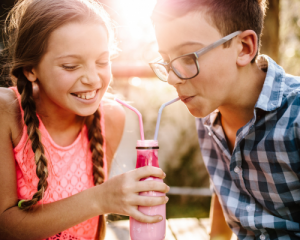 girl and boy enjoy a beverage flavor as they drink from straws in a shared bottle smiling 